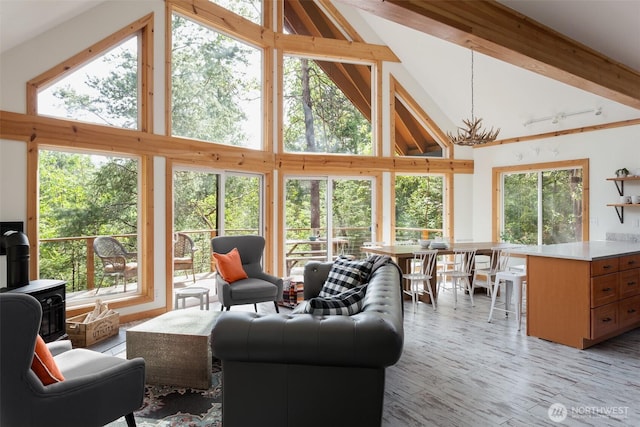 living area with a wood stove, a healthy amount of sunlight, high vaulted ceiling, and beamed ceiling