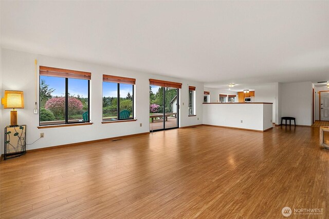 unfurnished living room featuring plenty of natural light, baseboards, and wood finished floors