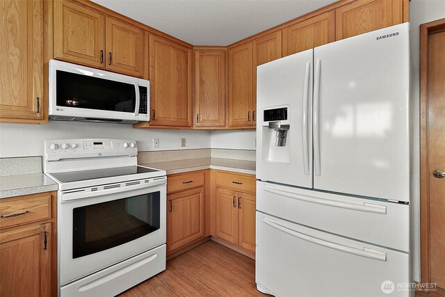 kitchen with light wood-type flooring, light countertops, brown cabinetry, and white appliances