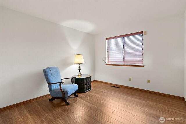 living area with visible vents, baseboards, and wood finished floors