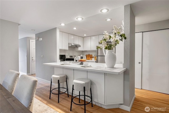 kitchen featuring white cabinetry, a peninsula, under cabinet range hood, stainless steel appliances, and light wood-style flooring
