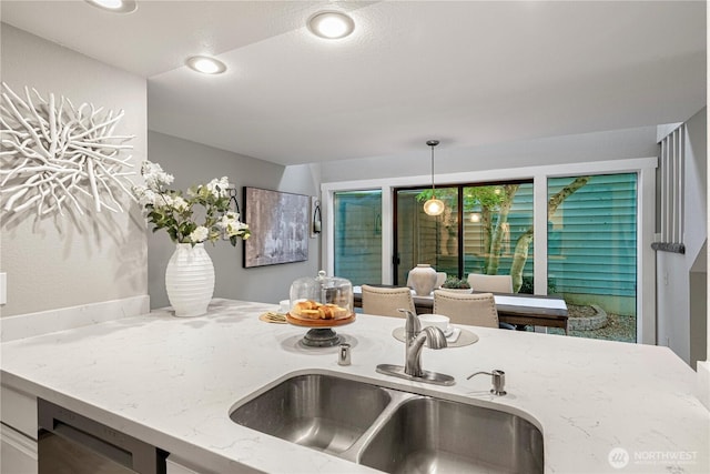 kitchen featuring pendant lighting, recessed lighting, light stone counters, a sink, and dishwasher