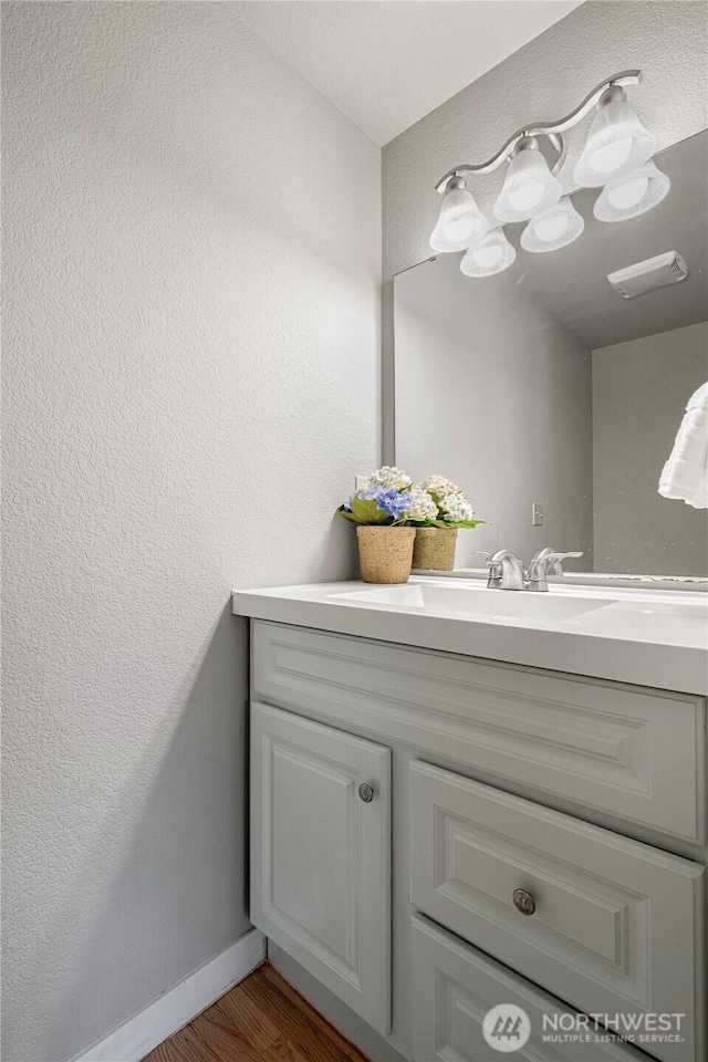 bathroom with vanity, visible vents, a textured wall, wood finished floors, and baseboards