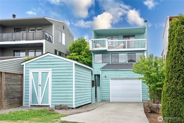 view of front facade featuring an attached garage, a storage shed, an outbuilding, a balcony, and driveway