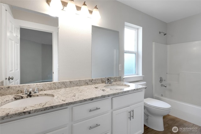 full bath with toilet, double vanity, a sink, and wood finished floors