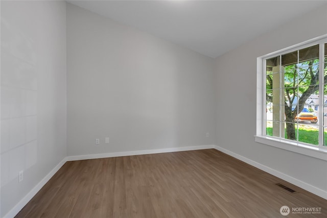 unfurnished room featuring baseboards, visible vents, and wood finished floors