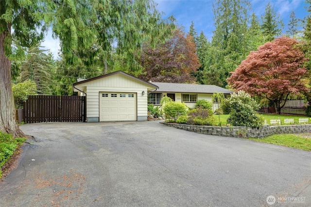 ranch-style house featuring a garage, aphalt driveway, and fence