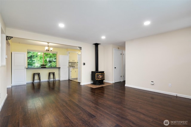 unfurnished living room featuring baseboards, a wood stove, dark wood-style flooring, and a chandelier