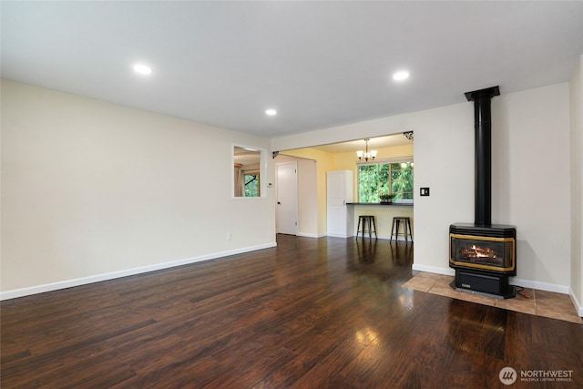unfurnished living room with a notable chandelier, a wood stove, recessed lighting, baseboards, and wood finished floors
