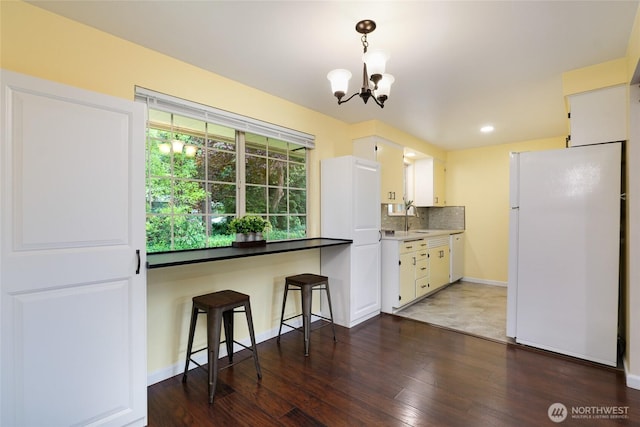 kitchen with a sink, white appliances, dark wood-style floors, and a chandelier