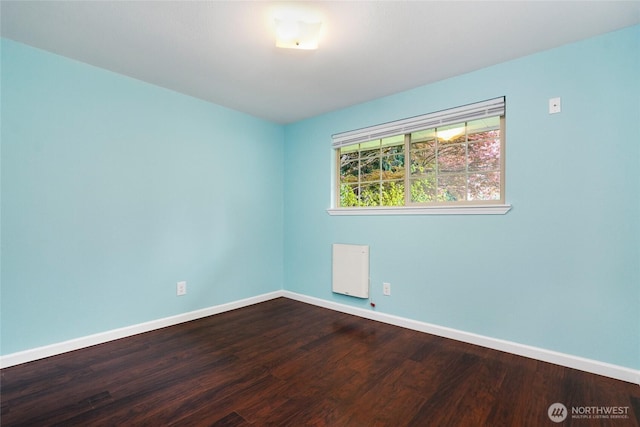 spare room featuring baseboards and dark wood-type flooring