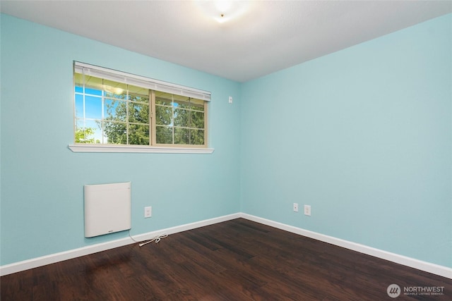 empty room with radiator heating unit, baseboards, and dark wood finished floors
