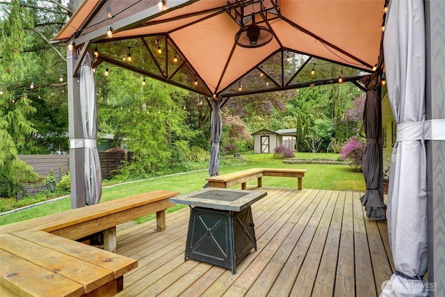 wooden deck with a gazebo, a storage shed, a lawn, an outdoor structure, and a fire pit
