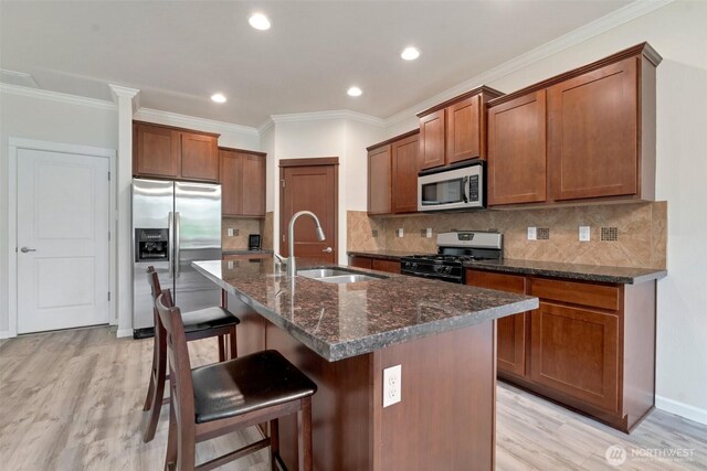 kitchen with a kitchen breakfast bar, brown cabinets, a sink, light wood finished floors, and appliances with stainless steel finishes
