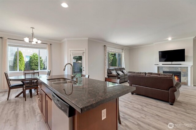 kitchen featuring stainless steel dishwasher, a fireplace, light wood-type flooring, a sink, and a chandelier