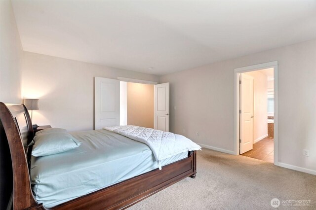 bedroom featuring baseboards, ensuite bath, and light colored carpet