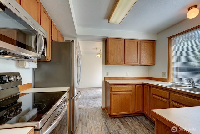kitchen with brown cabinetry, a sink, appliances with stainless steel finishes, and wood finished floors