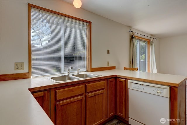 kitchen featuring brown cabinets, dishwasher, a sink, light countertops, and a peninsula