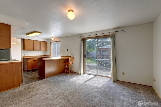 kitchen with brown cabinetry, a peninsula, dark carpet, a kitchen bar, and light countertops