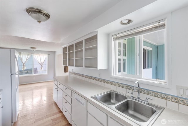 kitchen with a sink, light countertops, white cabinets, light wood finished floors, and white appliances