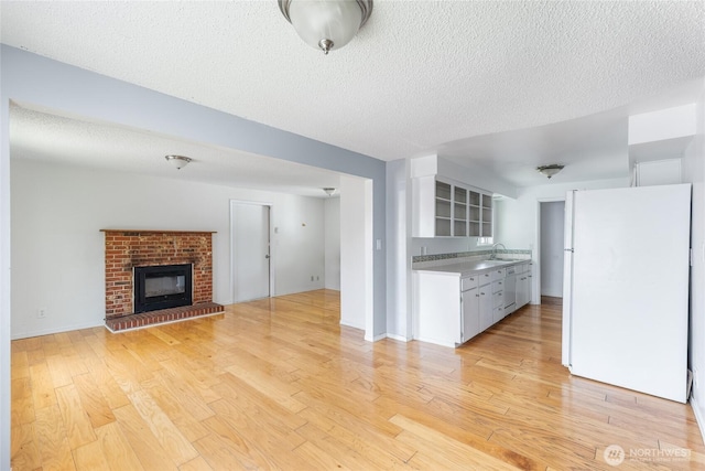 unfurnished living room featuring a sink, a textured ceiling, a fireplace, and light wood-style flooring