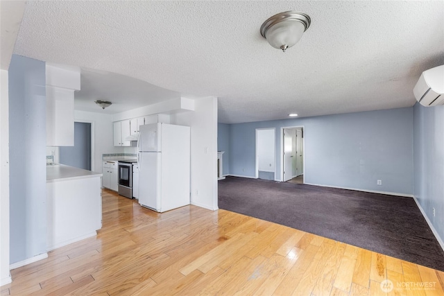 unfurnished living room featuring a textured ceiling, baseboards, a wall mounted AC, and light wood finished floors