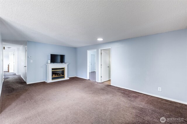 unfurnished living room with a textured ceiling, baseboards, a glass covered fireplace, and dark colored carpet
