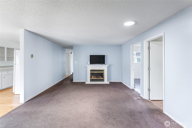 unfurnished living room with carpet flooring, a textured ceiling, and a glass covered fireplace
