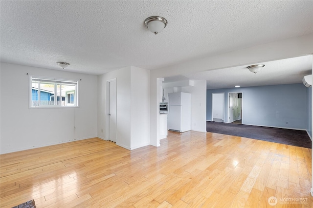 unfurnished living room featuring baseboards, a textured ceiling, and light wood finished floors