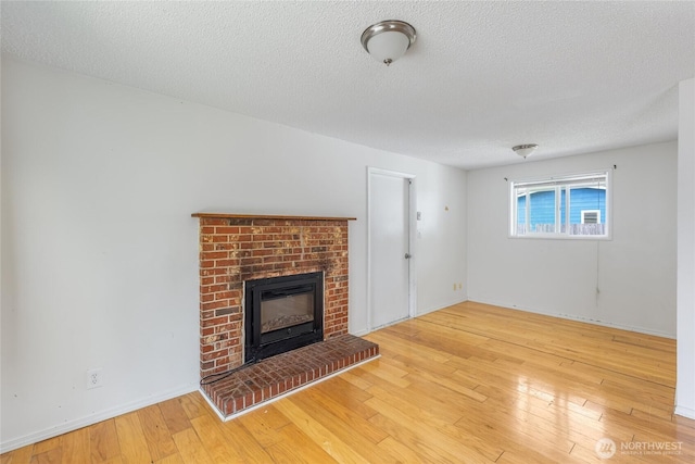 unfurnished living room with baseboards, a textured ceiling, a brick fireplace, and hardwood / wood-style floors