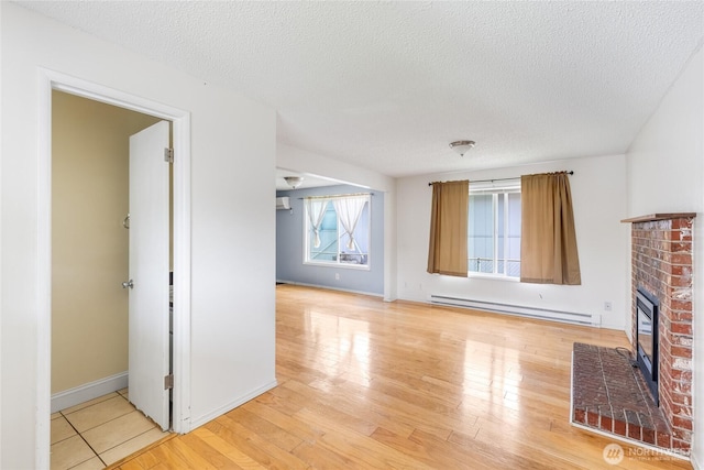 unfurnished living room featuring baseboards, a textured ceiling, baseboard heating, and light wood-style flooring