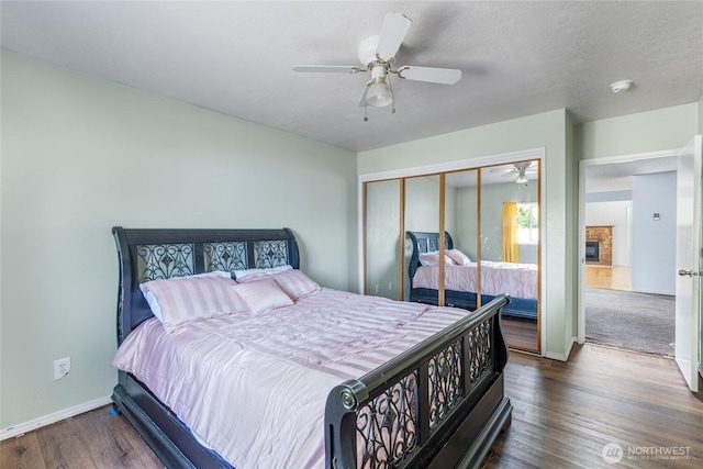 bedroom with a closet, a glass covered fireplace, wood finished floors, baseboards, and ceiling fan