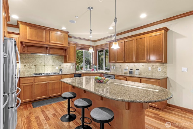 kitchen with brown cabinetry, a breakfast bar area, crown molding, appliances with stainless steel finishes, and light wood-style flooring