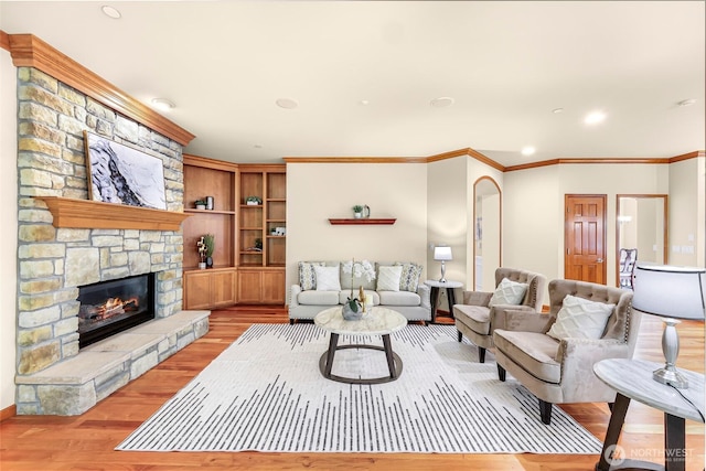 living area featuring ornamental molding, a stone fireplace, recessed lighting, and light wood-style flooring