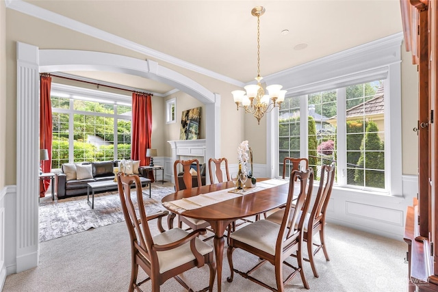 carpeted dining area with crown molding, wainscoting, a decorative wall, arched walkways, and a notable chandelier