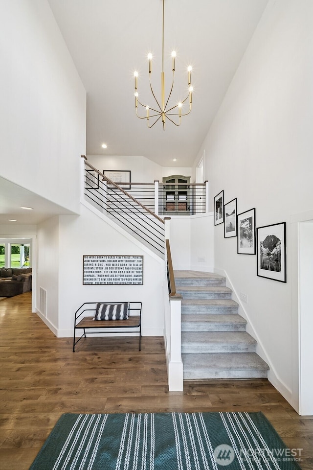 stairs featuring visible vents, a towering ceiling, wood finished floors, baseboards, and a chandelier