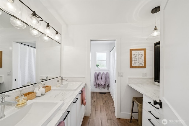full bathroom featuring double vanity, a sink, baseboards, and wood finished floors