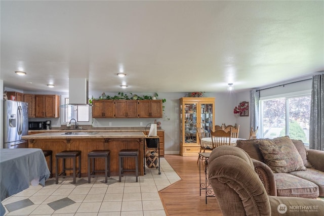 kitchen featuring brown cabinetry, stainless steel fridge with ice dispenser, light countertops, open floor plan, and a kitchen breakfast bar
