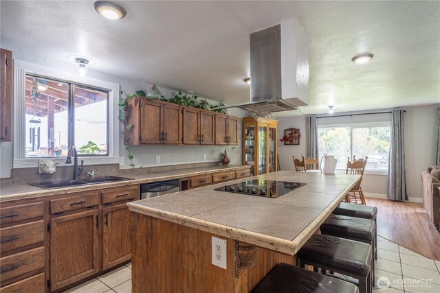 kitchen featuring brown cabinets, a sink, a kitchen bar, black electric cooktop, and island exhaust hood