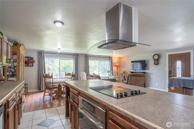 kitchen with black electric stovetop, tile counters, light tile patterned flooring, oven, and wall chimney exhaust hood
