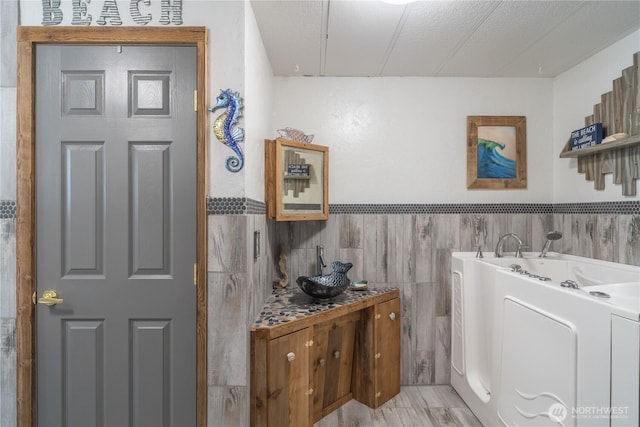 bathroom featuring a bath, tile walls, and wainscoting