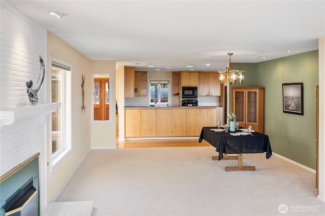kitchen featuring black microwave, a brick fireplace, baseboards, a chandelier, and light carpet