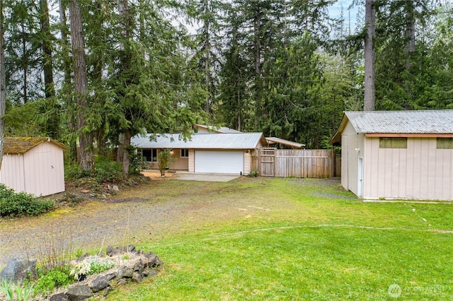 view of yard with a storage unit, fence, an outbuilding, a garage, and dirt driveway