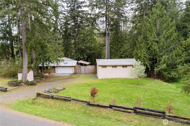 view of yard featuring a garage, an outbuilding, a shed, driveway, and fence
