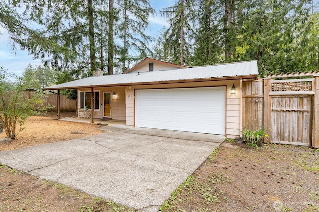 view of front of home featuring metal roof, driveway, a chimney, an attached garage, and fence