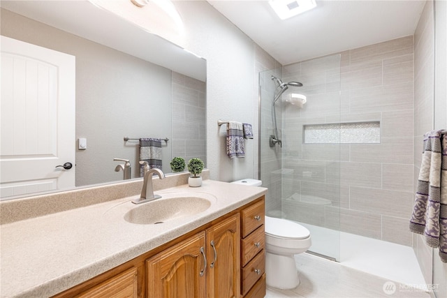 bathroom featuring a tile shower, toilet, and vanity