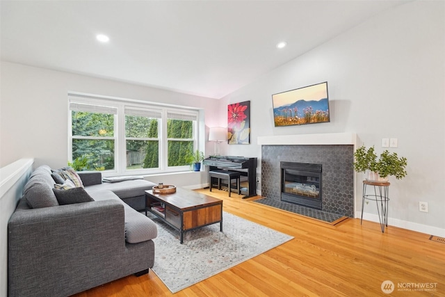 living room with baseboards, a fireplace with flush hearth, wood finished floors, and lofted ceiling