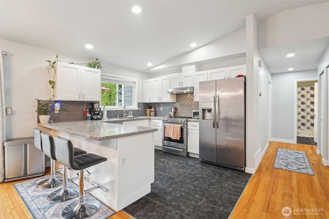 kitchen with white cabinets, stainless steel appliances, a peninsula, lofted ceiling, and under cabinet range hood