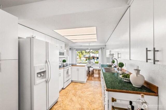 kitchen with a peninsula, white appliances, a chandelier, white cabinets, and a sink
