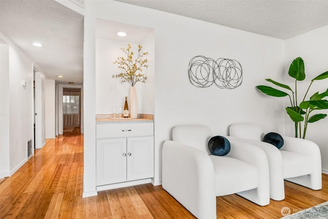 sitting room featuring a textured ceiling, visible vents, and light wood-type flooring